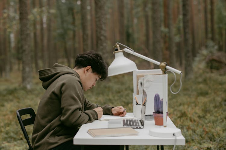 Man In A Green Jacket Writing On A Notebook