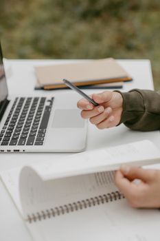 Close-up of hands using a pen alongside a laptop in a modern workspace.
