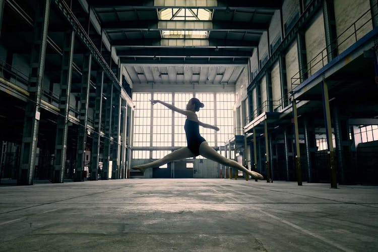 Low Angle View Of A Ballerina Midair In An Industrial Building