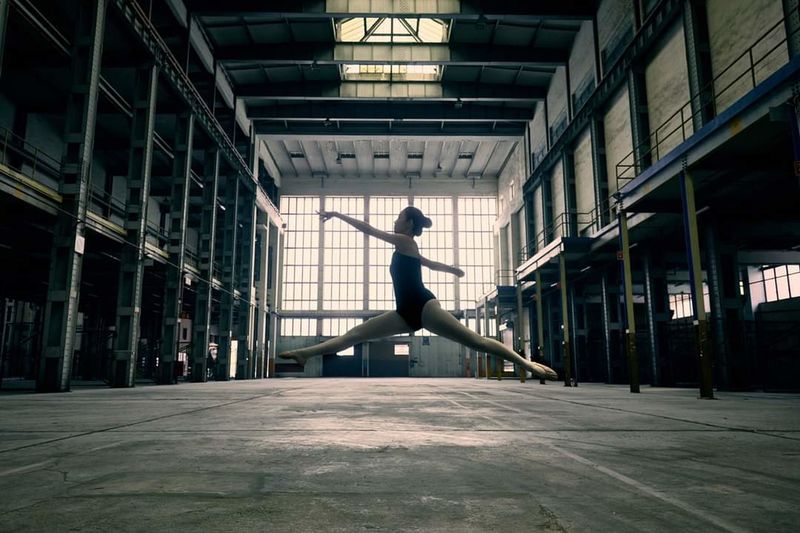 Composed frame: a dancer suspended mid-leap in a tall daylit warehouse — photo by Derrick Khuen on Pexels