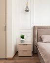 Bedside table with potted plant placed near comfortable bed with pink coverlet and pillows in cozy room at home