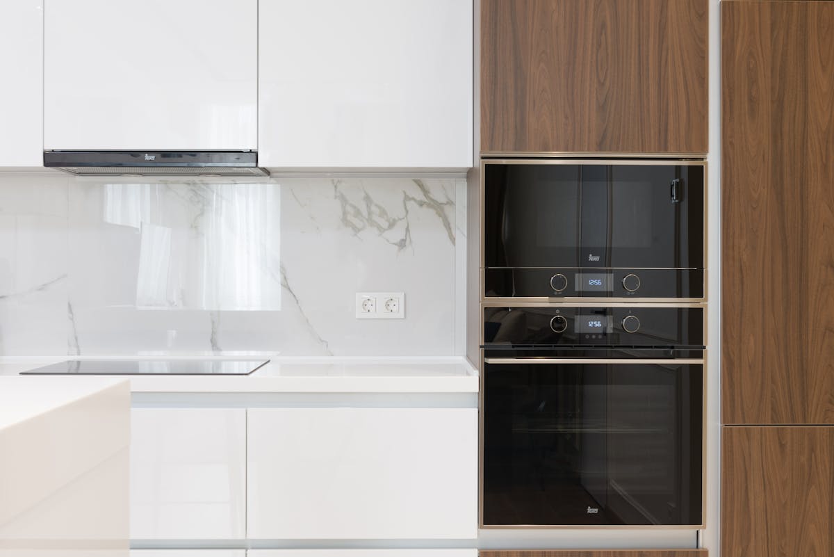 Modern interior of white and wooden kitchen with cabinets cupboards and built in appliances in contemporary flat