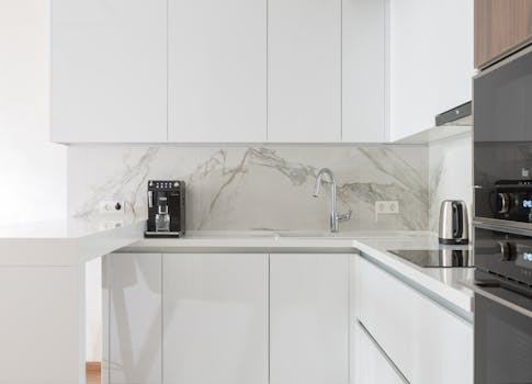 Sleek white kitchen interior with modern appliances and marble backsplash.