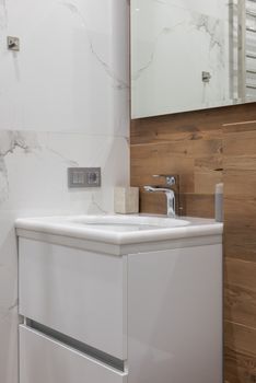 Interior of light bathroom with sink placed under big mirror with towel rail in reflection in modern apartment