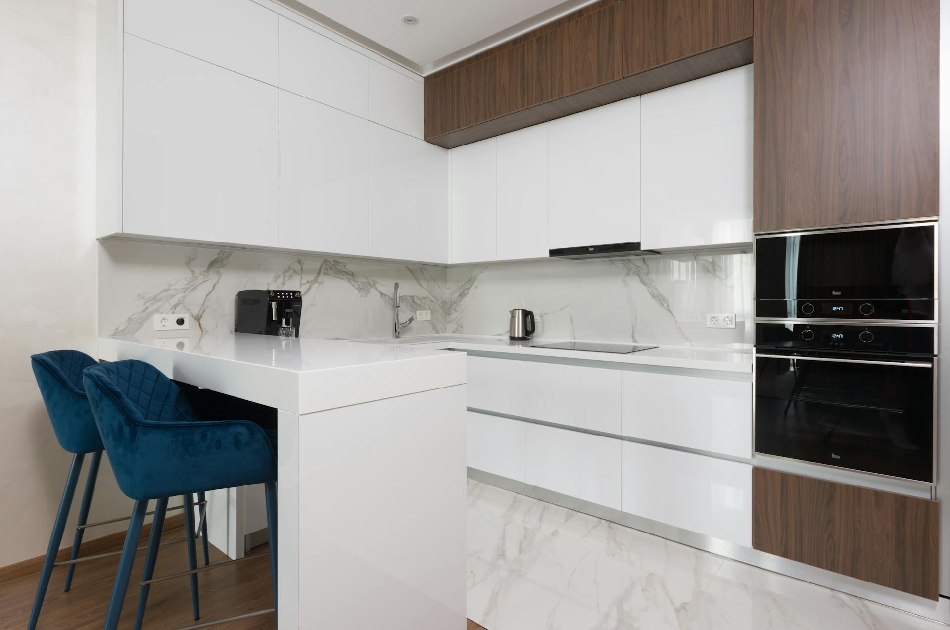 Interior of light modern kitchen with chairs at dining table and appliances placed in modern apartment