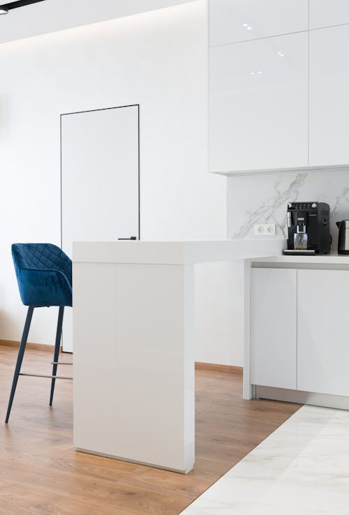 White counter with blue bar chair in spacious kitchen with minimalist furniture and modern appliances in daylight