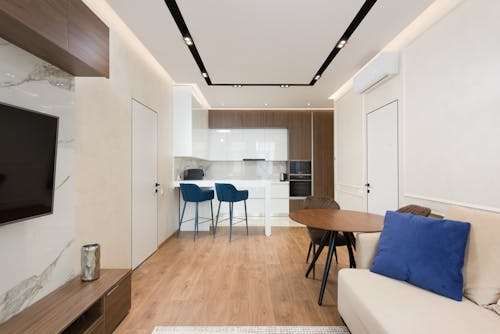 Interior of modern apartment with living room with comfy sofa and wooden furniture near kitchen zone with counter and white cabinets