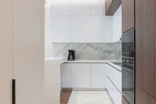 Minimalist interior of small kitchen with white and wooden cupboards and modern appliances in light apartment