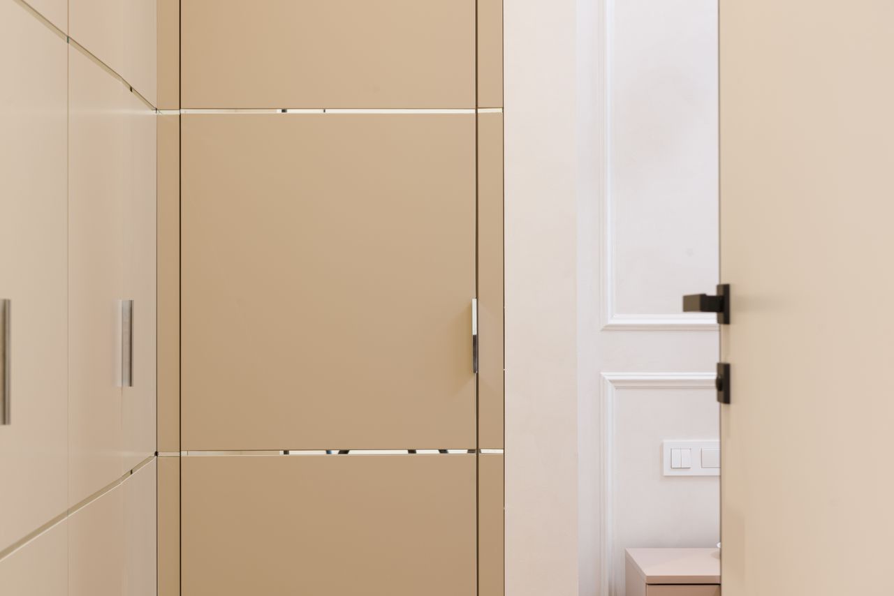 Beige fitted wardrobes with slim handles beside an open panelled door