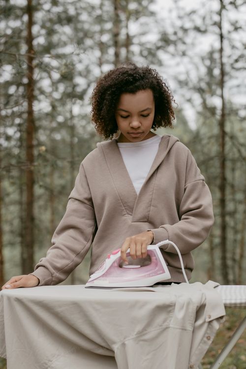 Free Young woman ironing clothes outdoors in a serene forest setting. Stock Photo