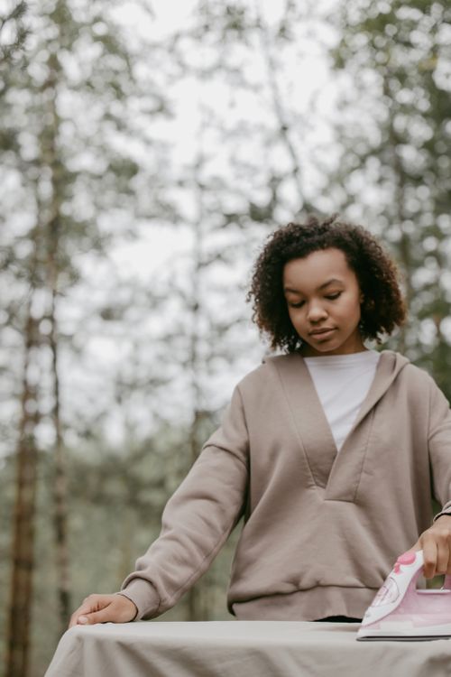 Free A young woman in a hoodie irons clothes on an outdoor ironing board. Stock Photo