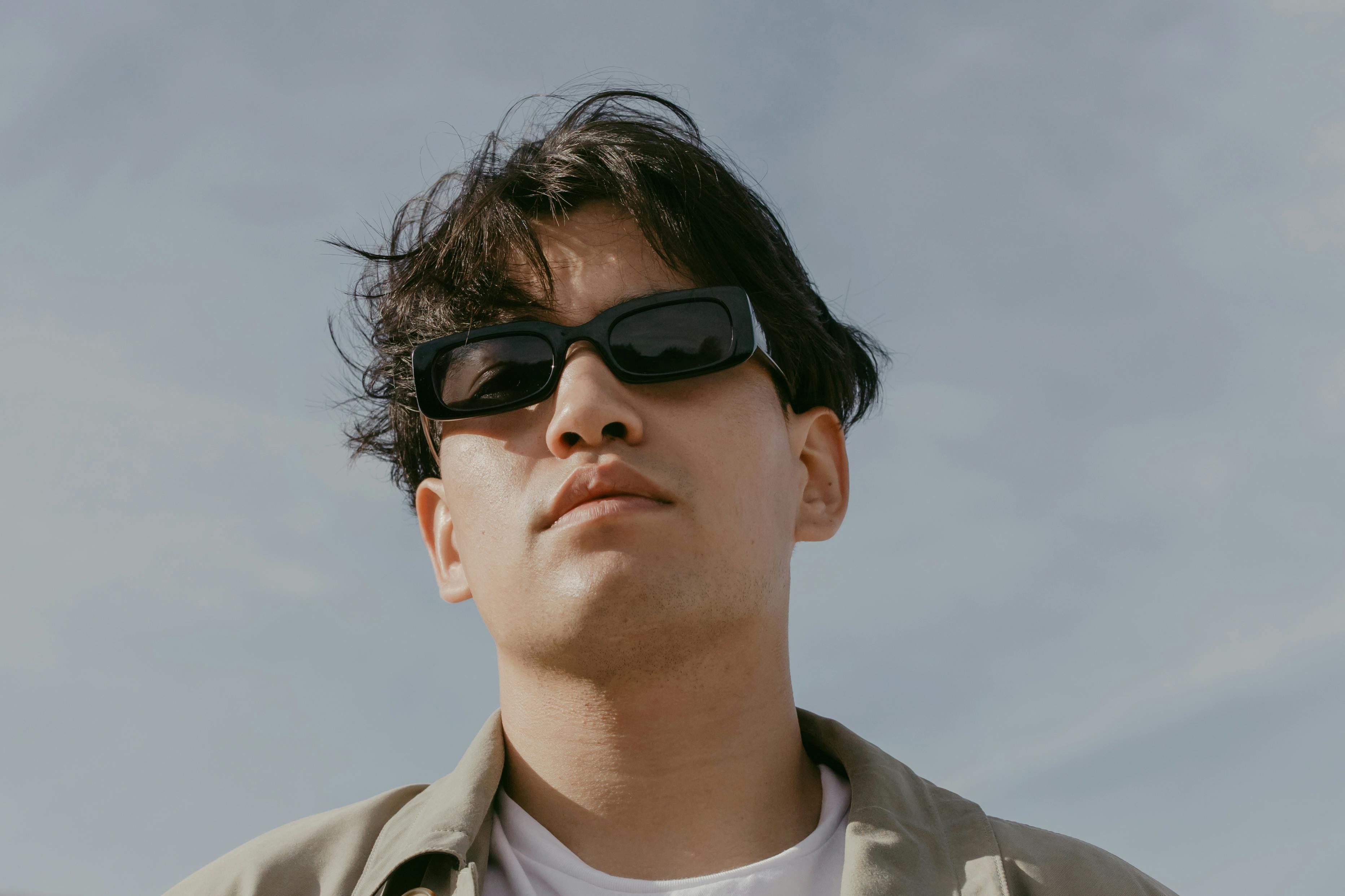 Portrait of a stylish man wearing sunglasses outdoors on a sunny day under clear skies.