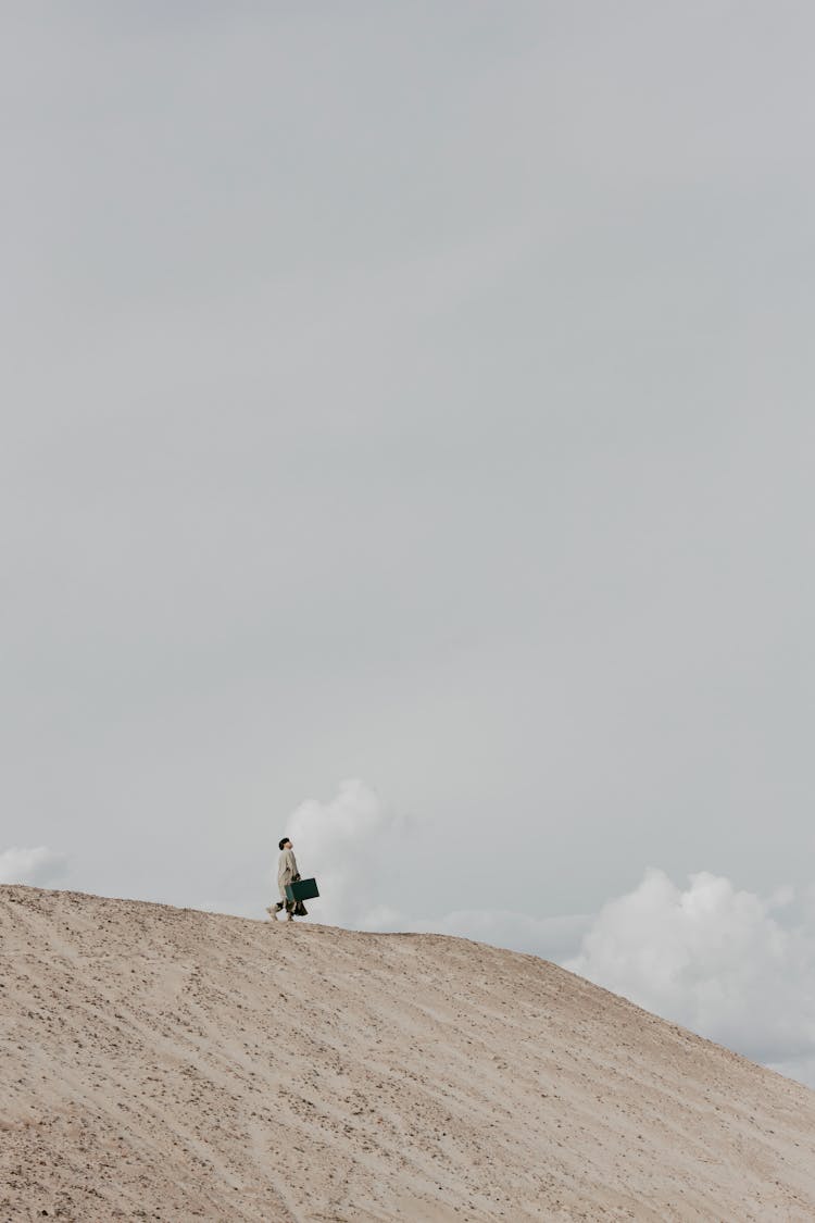 Man Walking On Dry Land Under Gray Sky With A Luggage