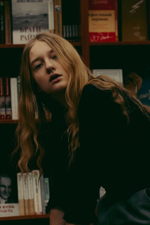 Stylish young woman spending time in library and looking at camera