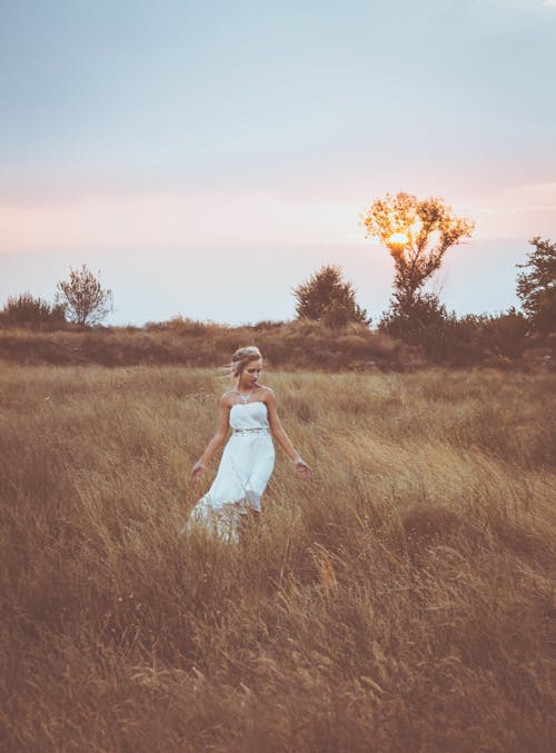 Graceful female walking on grassy meadow at sunset