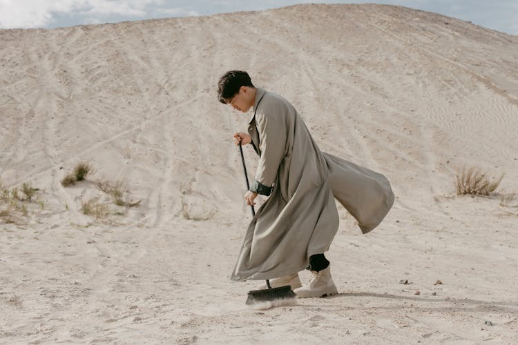 A Man Using A Broom In A Desert