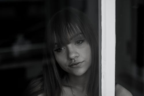 A Grayscale Photo of a Woman Looking at the Window