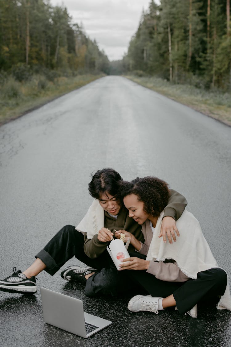 A Couple Sitting On The Road While Eating Food