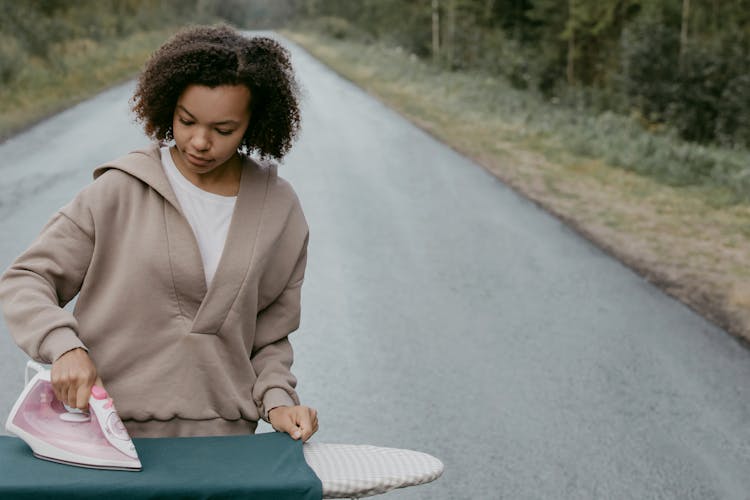 A Woman In Jacket Ironing Clothes In The Middle Of The Road