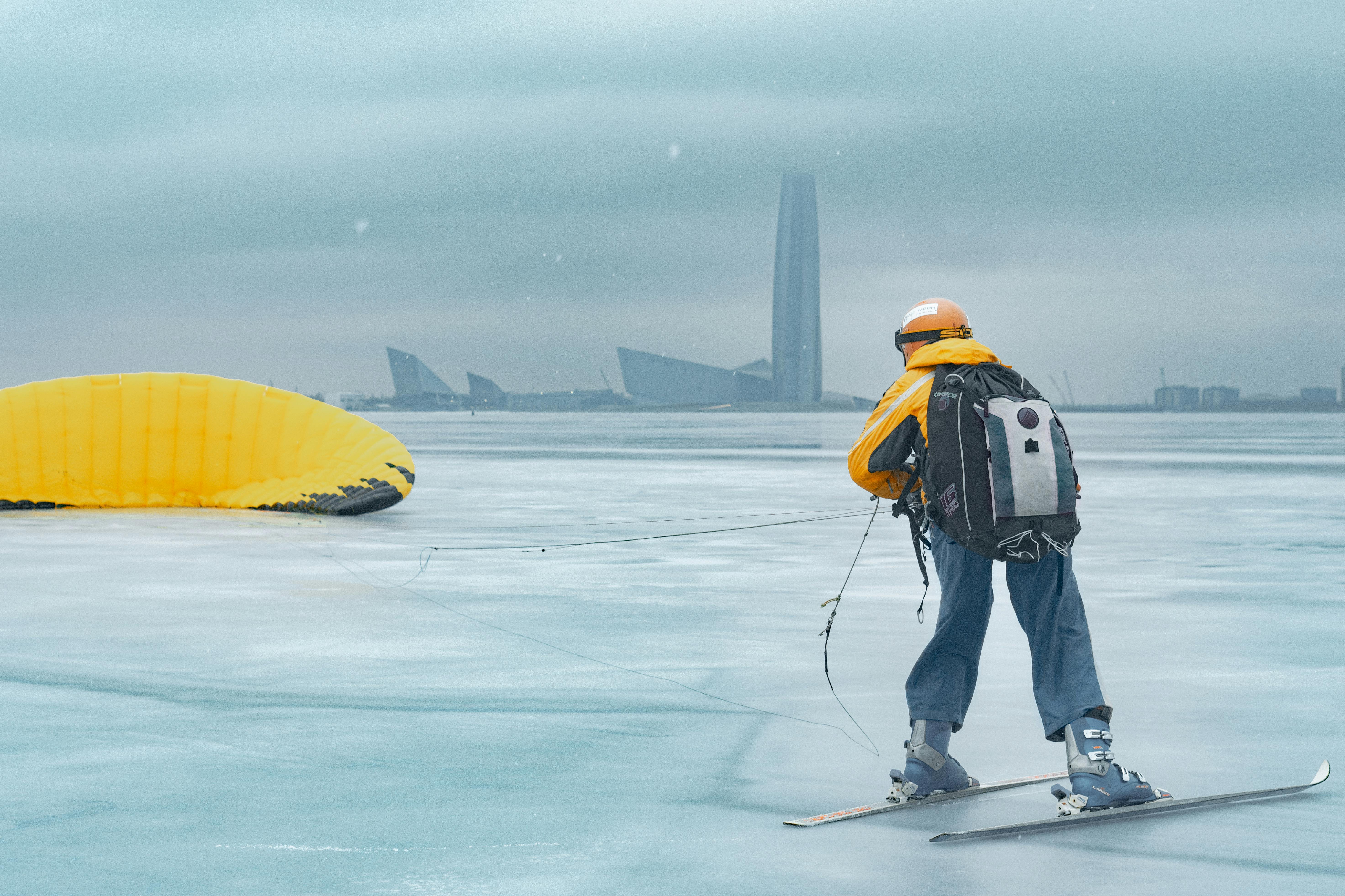 Person snowkiting on a frozen lake in Saint Petersburg with cityscape in background.