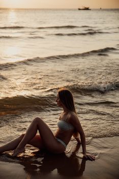 Serene scene of a woman sitting on a sandy beach at sunset, waves gently lapping onshore.