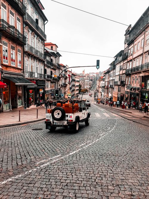 Free A jeep drives along a historic cobblestone street in Porto, showcasing urban architecture. Stock Photo
