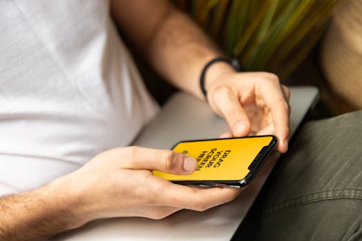 Close-up of a person holding a smartphone with a yellow screen while sitting indoors.