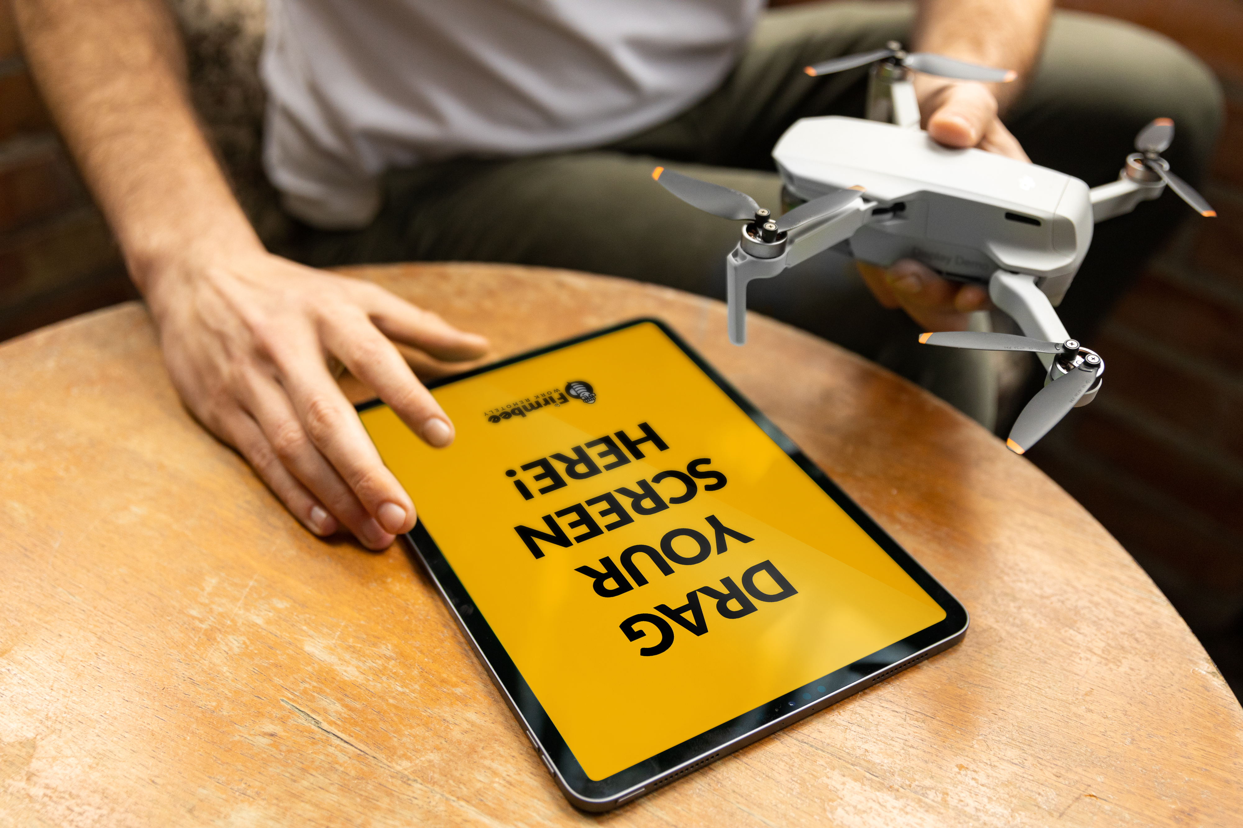 Person holding drone next to a tablet with a yellow screen on a wooden table.