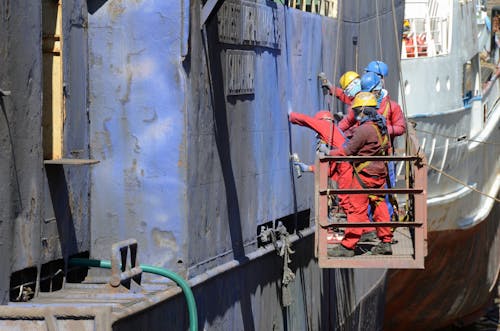 Men on a Hanging Platform Repairing the Outside of a Ship in a Shipyard