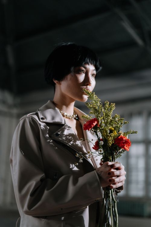 Free Thoughtful woman with short hair holding flowers in indoor setting. Stock Photo