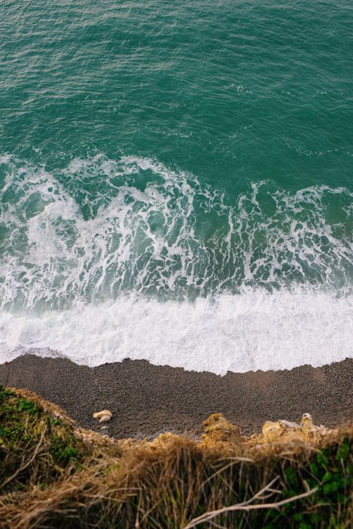 Free Aerial view of ocean waves crashing on a secluded pebble beach with vibrant greenery. Stock Photo