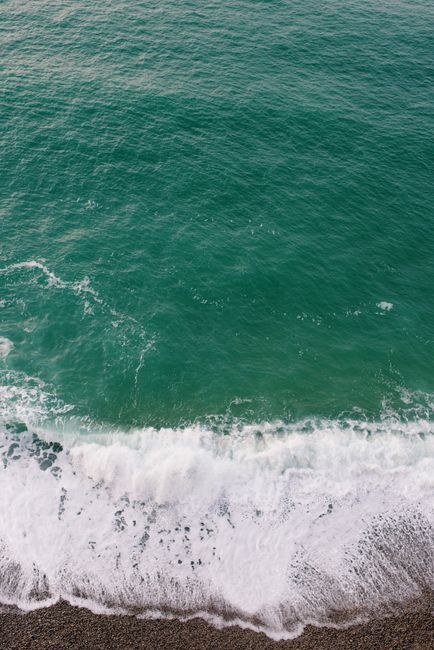 Tranquil ocean waves with foam gently wash over a pebble beach, creating a serene coastal scene.
