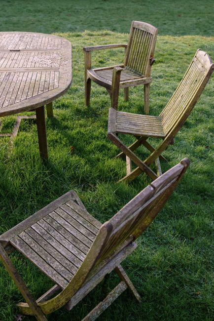 A set of weathered wooden chairs and table on a grassy lawn, conveying rustic charm.
