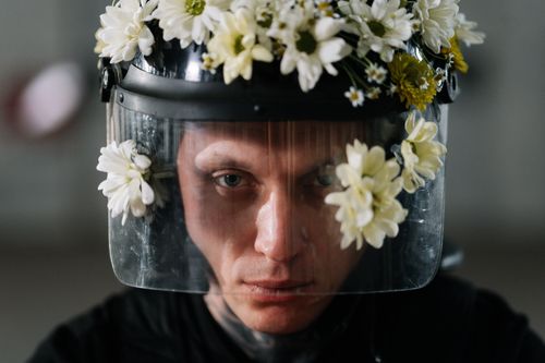 Free A protester in riot gear wears a helmet adorned with flowers as a symbol of peaceful protest. Stock Photo