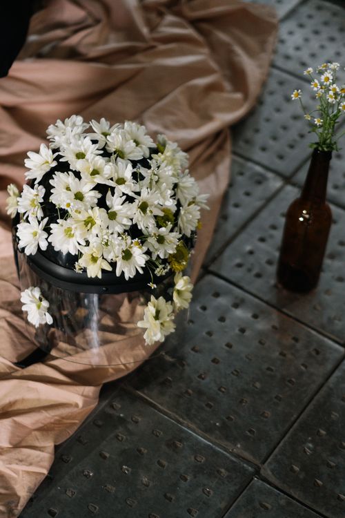 Free A creative arrangement of daisies on a helmet beside a flower vase on a metal floor. Stock Photo