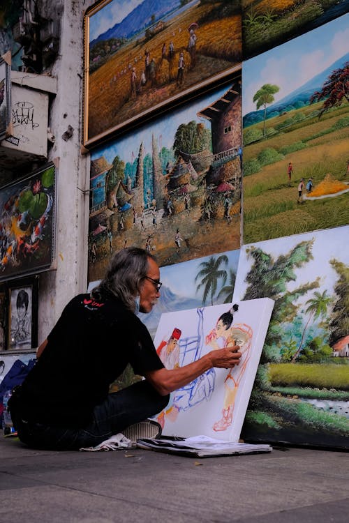 Street Artist Sitting on Pavement and Painting Pictures
