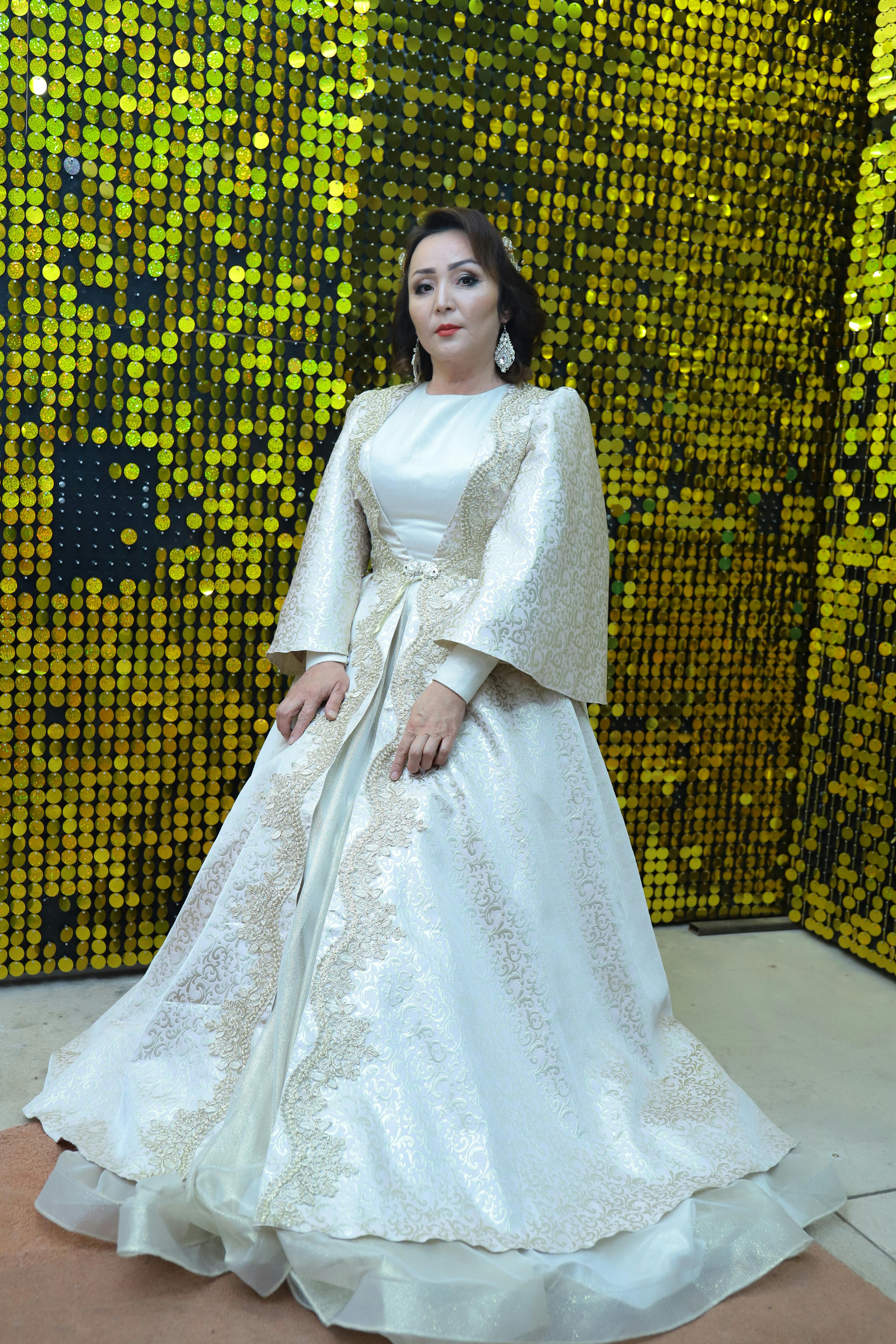 Elegant woman in a detailed bridal gown posing against a sparkling sequin backdrop.