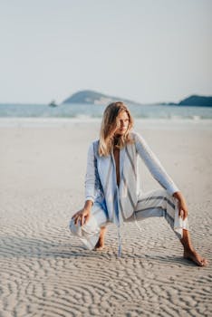 Fashionable woman poses in striped attire on a serene Bali beach during a sunny day.