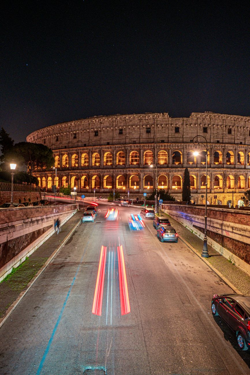 Roma di notte con le luci del traffico davanti al Colosseo