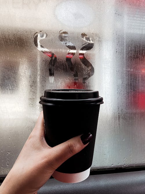 Free Hand woman holding cup of takeaway coffee near misted window Stock Photo