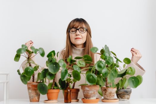 Woman practicing meditation surrounded by lush green indoor plants on a white background.