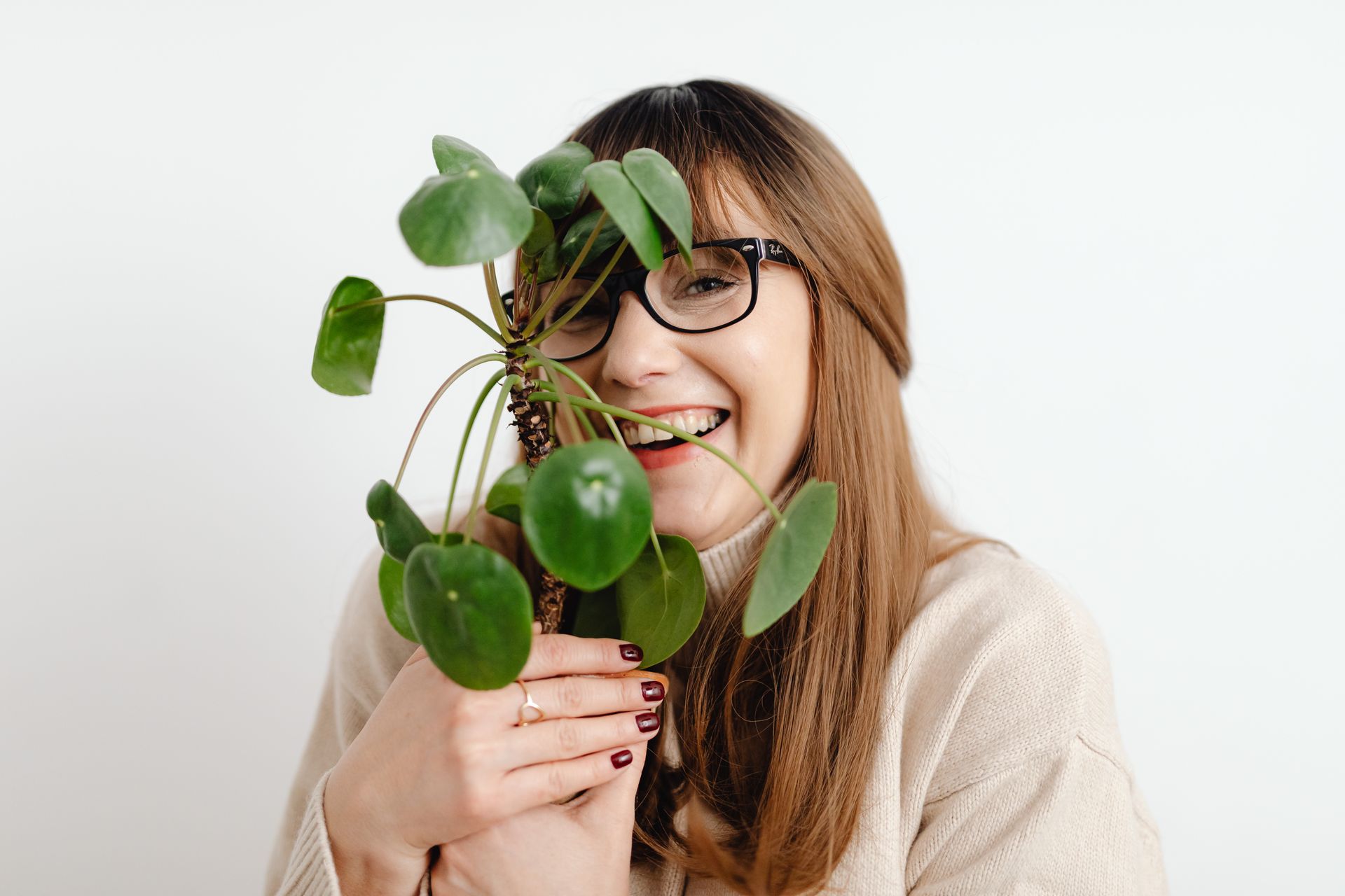 Smiling woman happily embracing a Chinese money plant in a bright indoor setting.