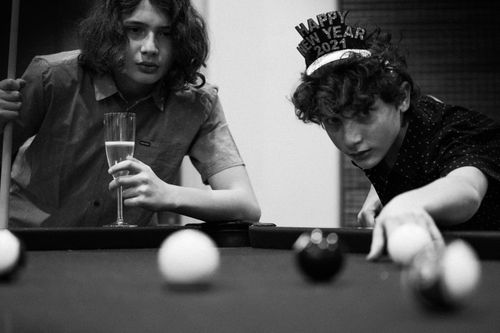 Free Two teenagers playing pool and celebrating New Year's Eve indoors. One holds champagne. Stock Photo