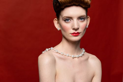 Free A stylish portrait of a woman with pearl jewelry, set against a vibrant red studio background. Stock Photo