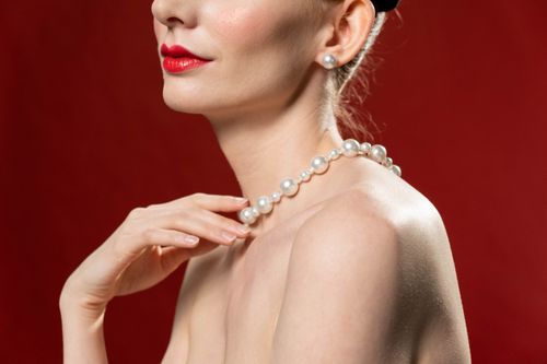Free Close-up of a woman wearing a pearl necklace, highlighting elegance and sophistication against a red backdrop. Stock Photo