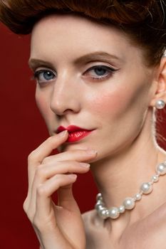 Close-up of a woman with pearls, red lips, and elegant makeup.