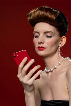 Elegant woman in pearls uses a smartphone in a studio setting.