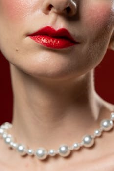 Elegant close-up portrait featuring red lipstick and a pearl necklace against a rich red background.