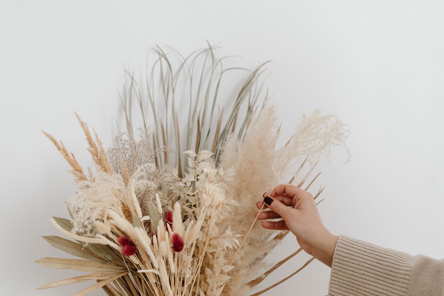 A close-up of a hand arranging a bouquet of dried flowers showcasing natural textures.