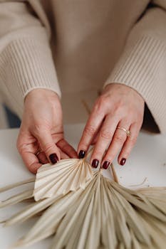 Hands with manicured nails arranging dried palm leaves creatively, close-up view.